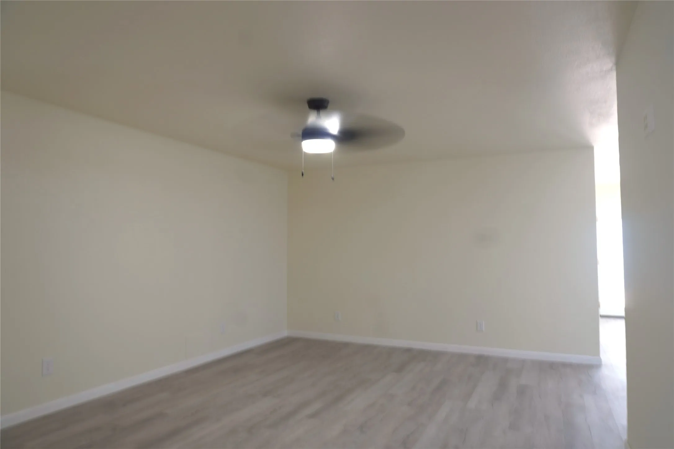 Spacious room with wood-finish flooring, a ceiling fan with integrated lighting, and neutral wall tones