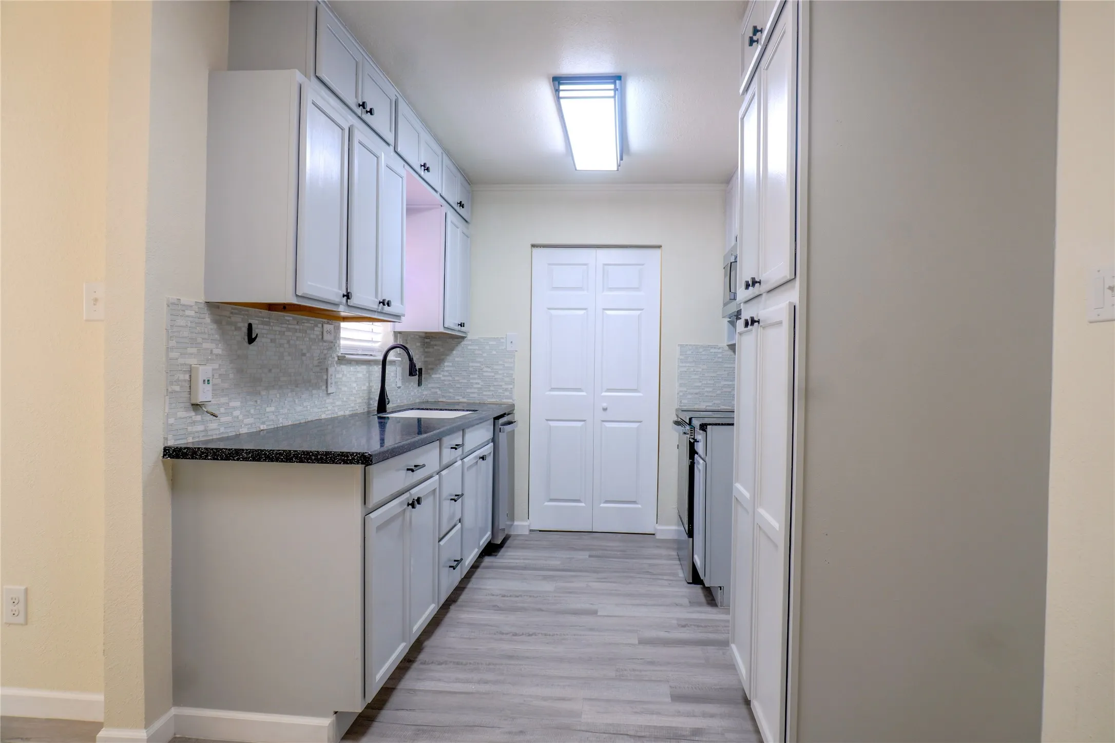 Galley kitchen featuring light gray cabinetry, dark countertops, a tiled backsplash, and wood-finish flooring