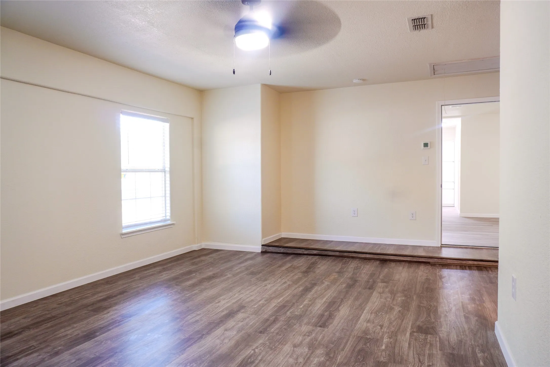 Wood-finish flooring, ceiling fan with integrated lighting, window with blinds, and light-toned wall finishes
