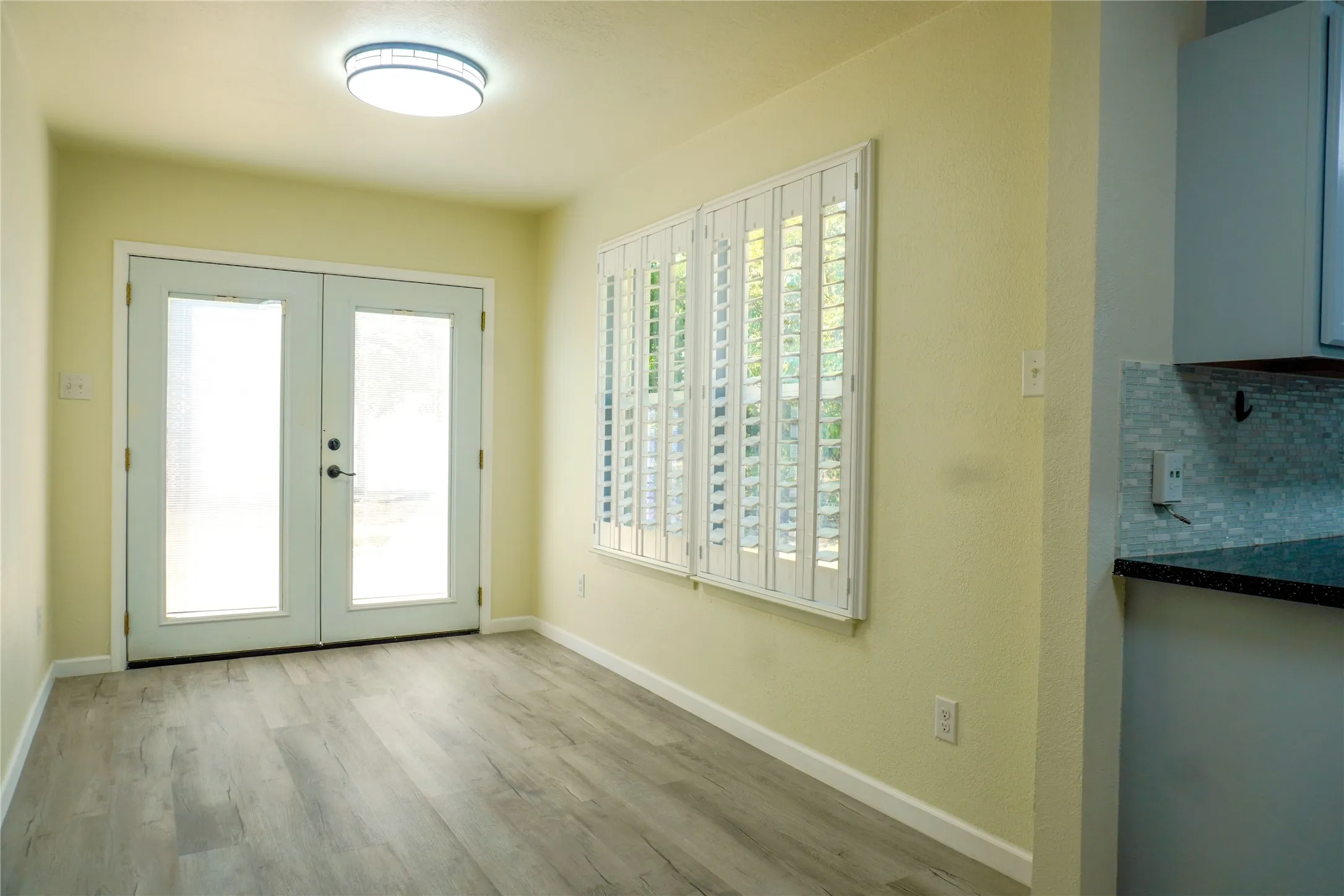 Wood-finish flooring, plantation shutters, double French doors, flush mount ceiling light, and subway tile backsplash