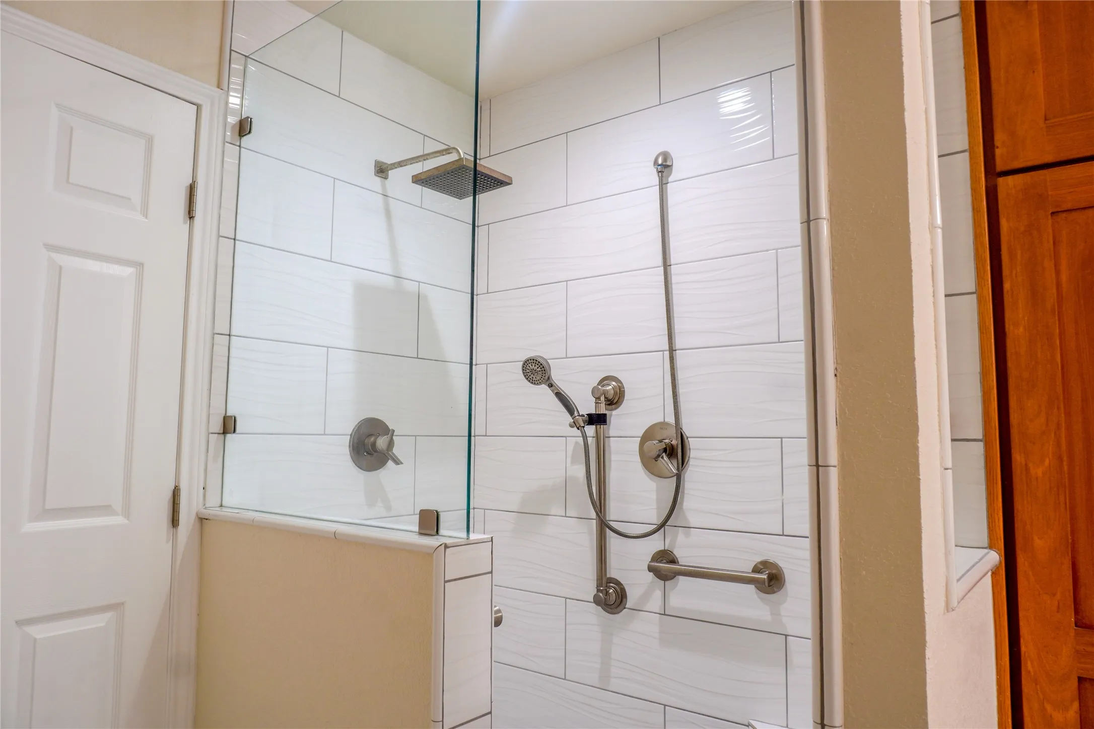 Glass-enclosed shower with white tiled walls, square rainfall showerhead, and handheld shower fixture
