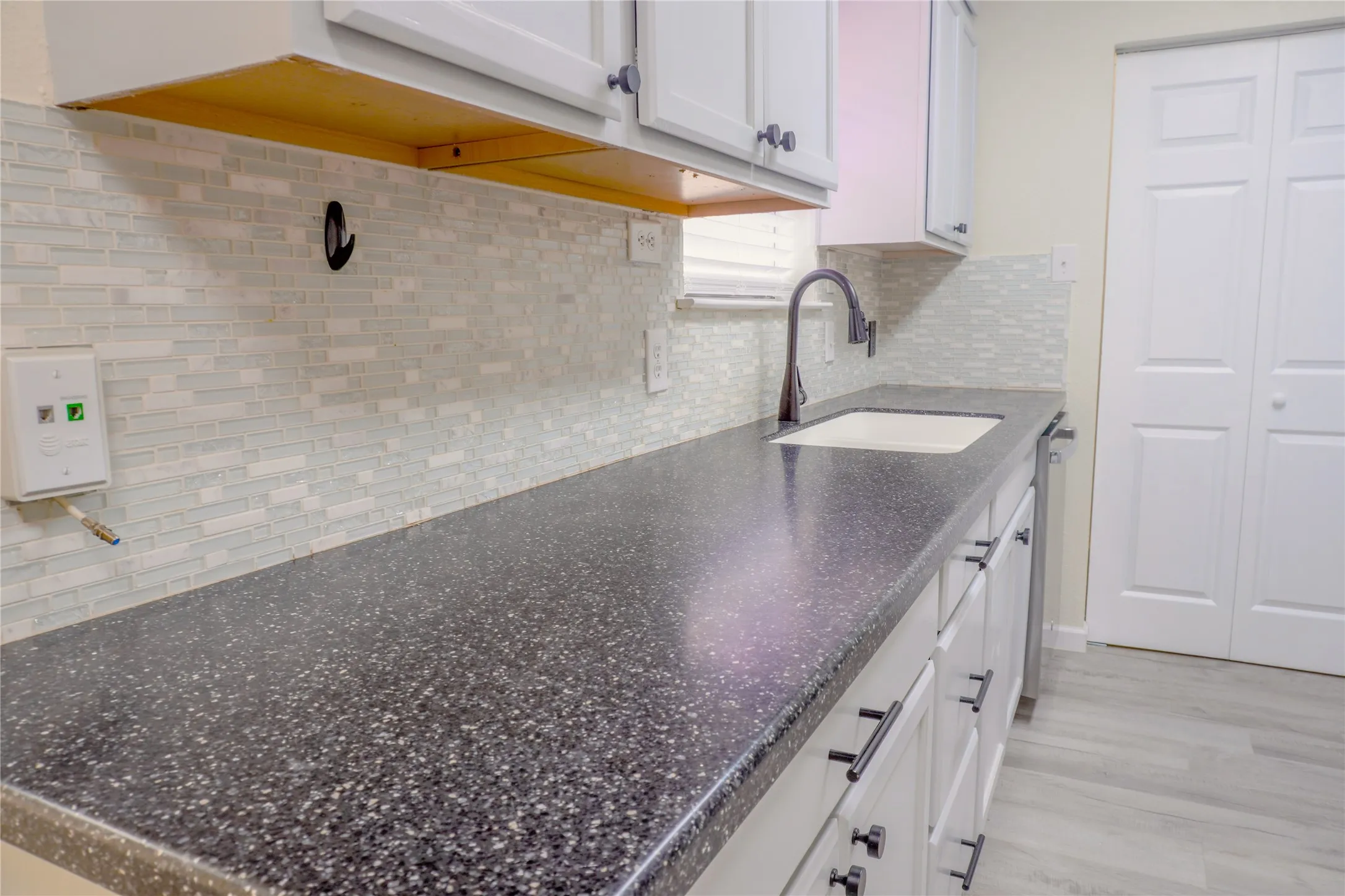 Quartz-finish countertop, white shaker-style cabinetry, mosaic tile backsplash, gooseneck faucet, and light wood-finish flooring