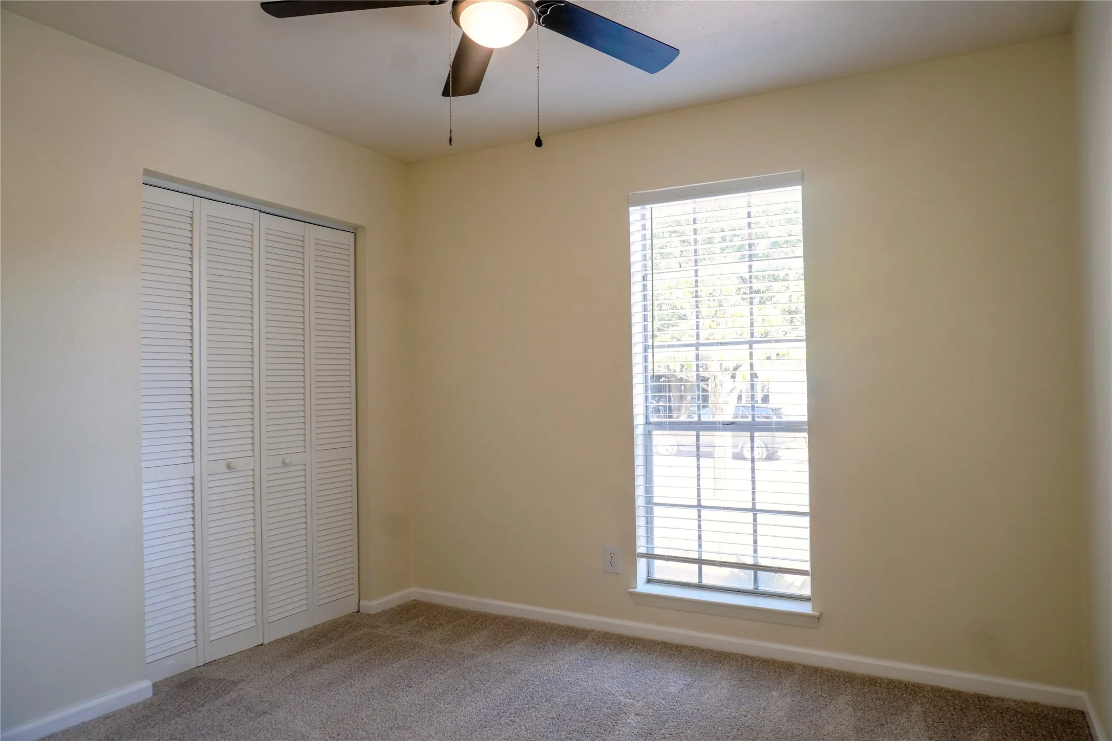 Recessed window with horizontal blinds, bi-fold louvered closet doors, ceiling fan with integrated lighting, and carpeted flooring