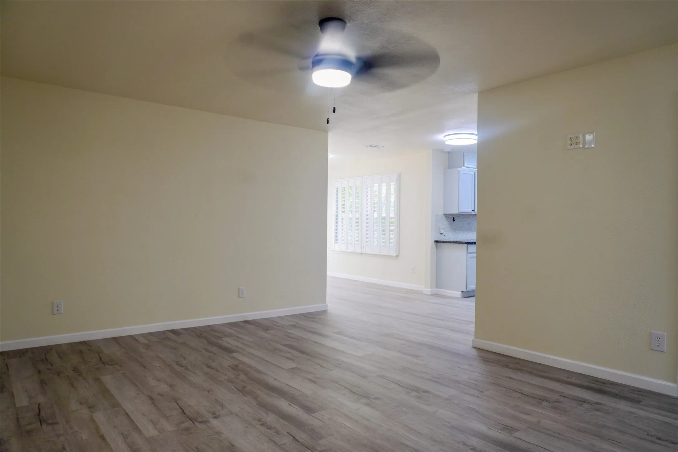 Wood-finish flooring, ceiling fan, neutral wall paint, recessed lighting, and plantation shutters