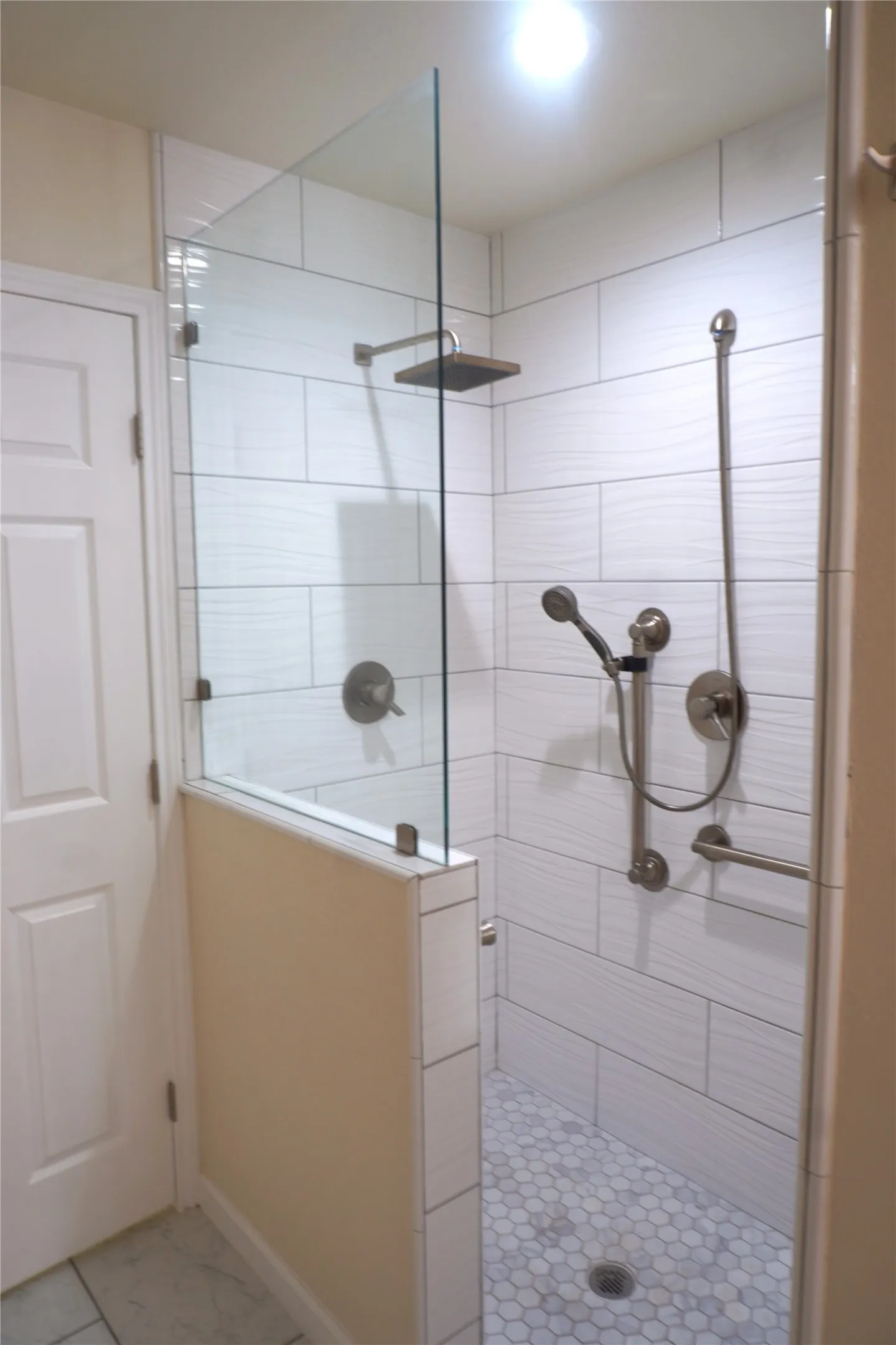 Walk-in shower with clear glass enclosure, white rectangular wall tiles, hexagonal floor tiles, and brushed nickel fixtures