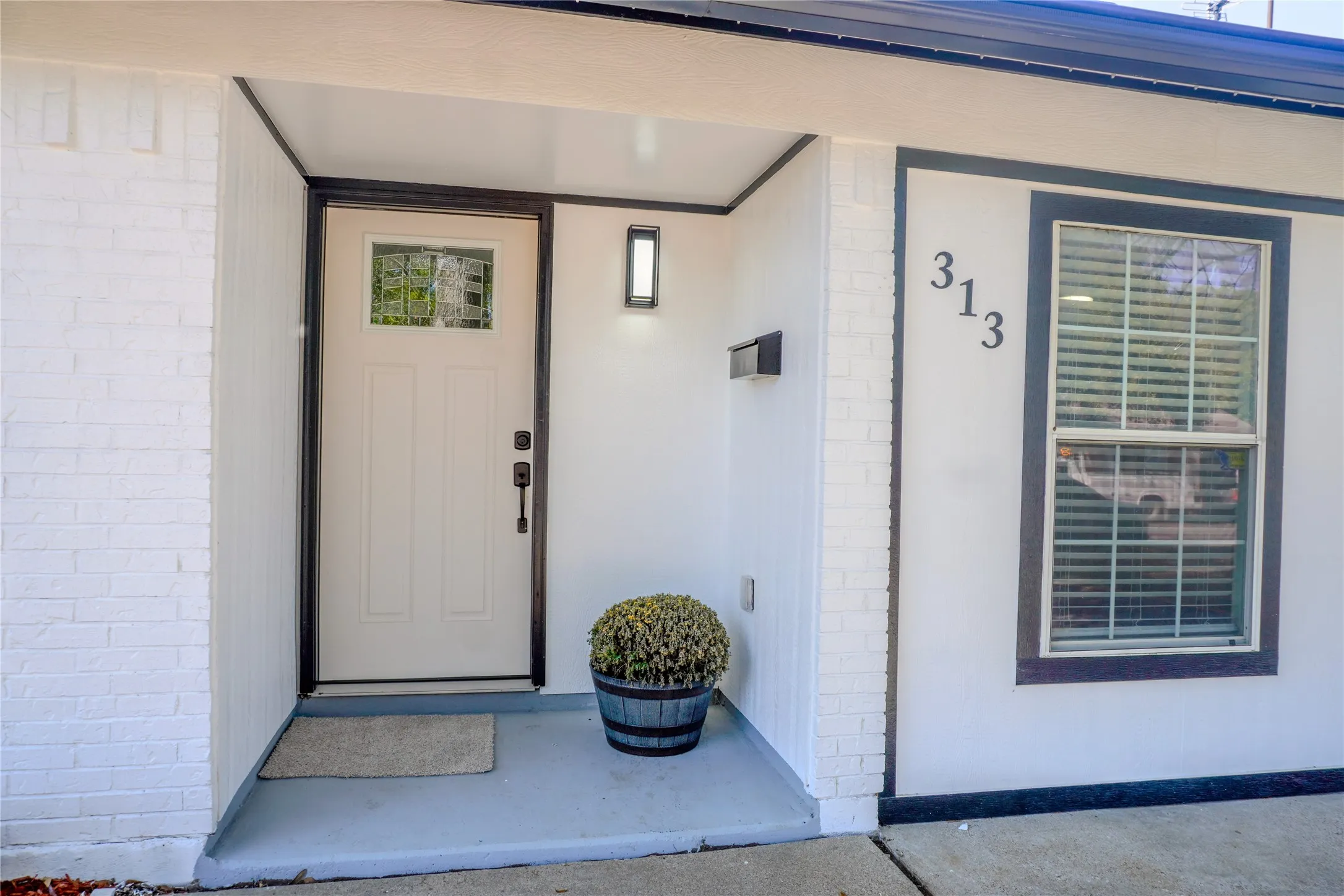 Inviting front entry featuring a paneled door with leaded glass, an exterior wall sconce, and a front-facing window with blinds