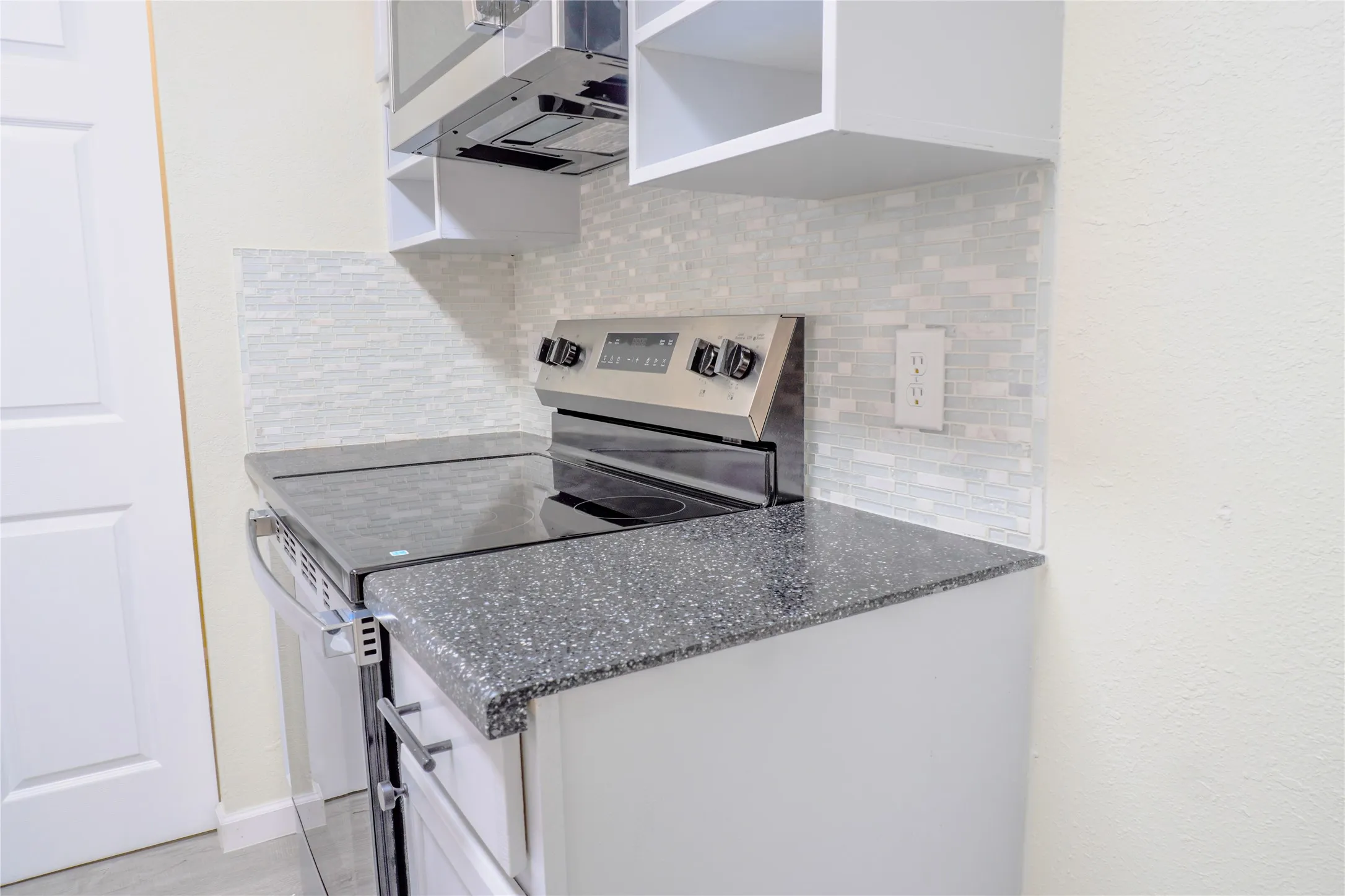 Stainless steel range with a flat cooktop, complemented by a mosaic tile backsplash and speckled countertops