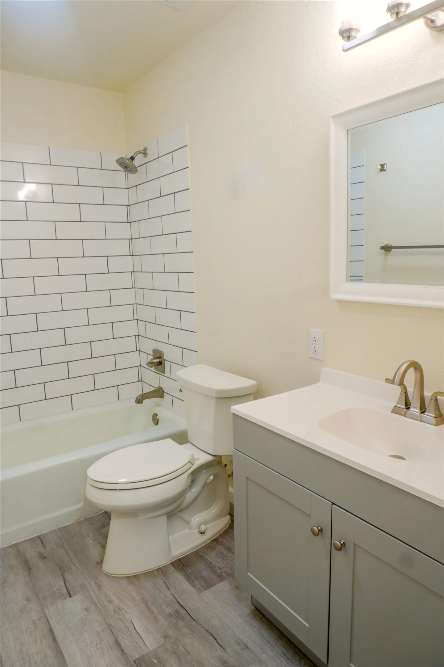 White subway tile shower surround, gray vanity with white countertop, chrome fixtures, and wood-finish flooring