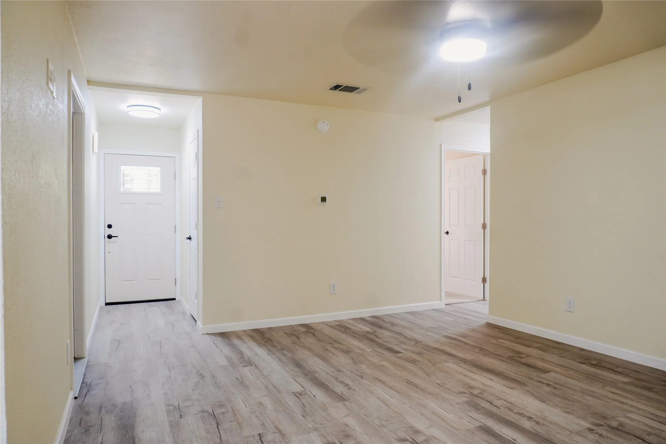 Expansive room with wood-finish flooring, a contemporary ceiling fan with integrated lighting, and a white paneled entry door with frosted glass