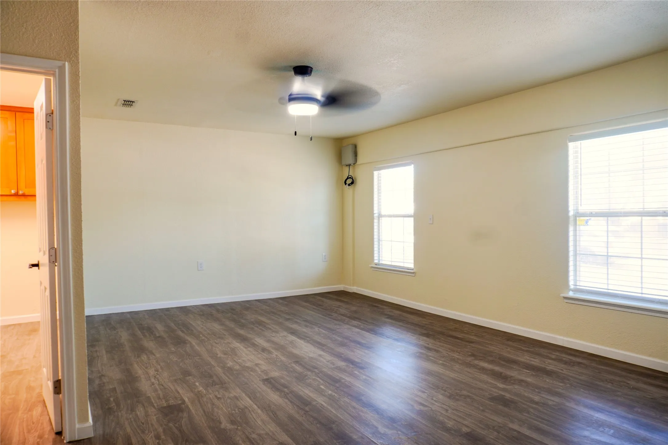 Spacious interior room with wood-finish flooring, two windows with blinds, and a ceiling fan