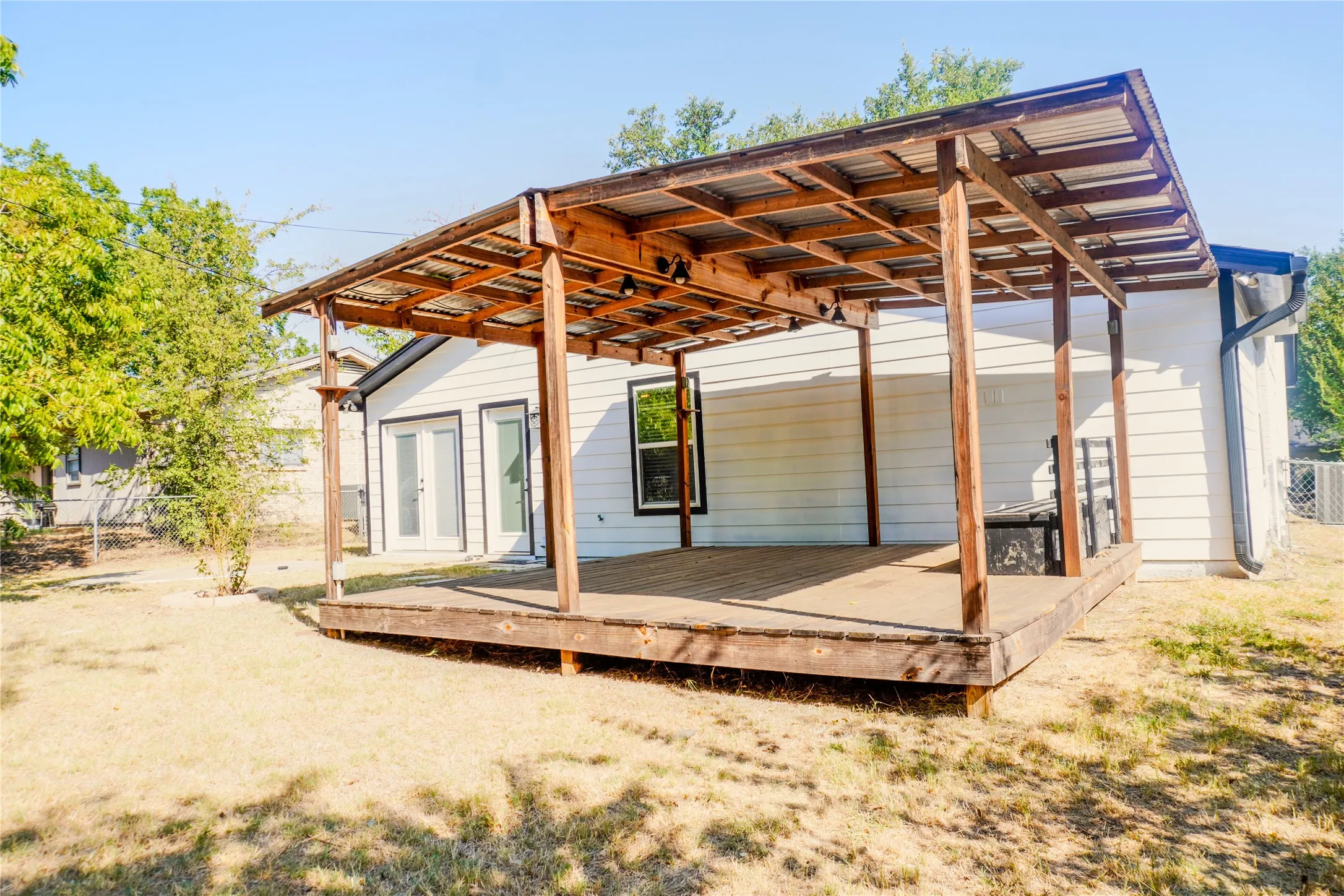 Expansive backyard featuring a wood deck with a covered patio, white horizontal siding, and double glass-paneled doors