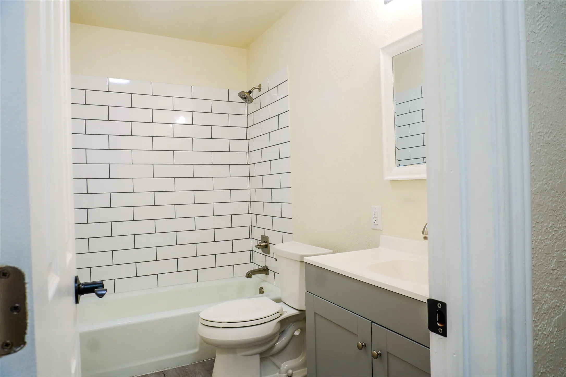 Bathroom featuring a subway tile shower surround, bathtub, toilet, vanity with integrated sink, and wall-mounted mirror