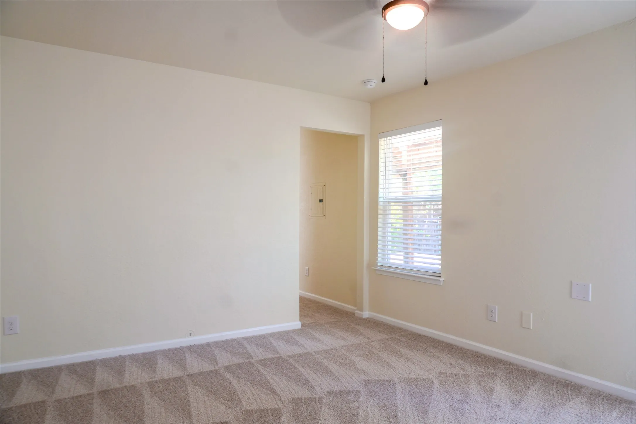 Textured carpet flooring, neutral painted walls, ceiling fan with integrated lighting, window with blinds, and white trim