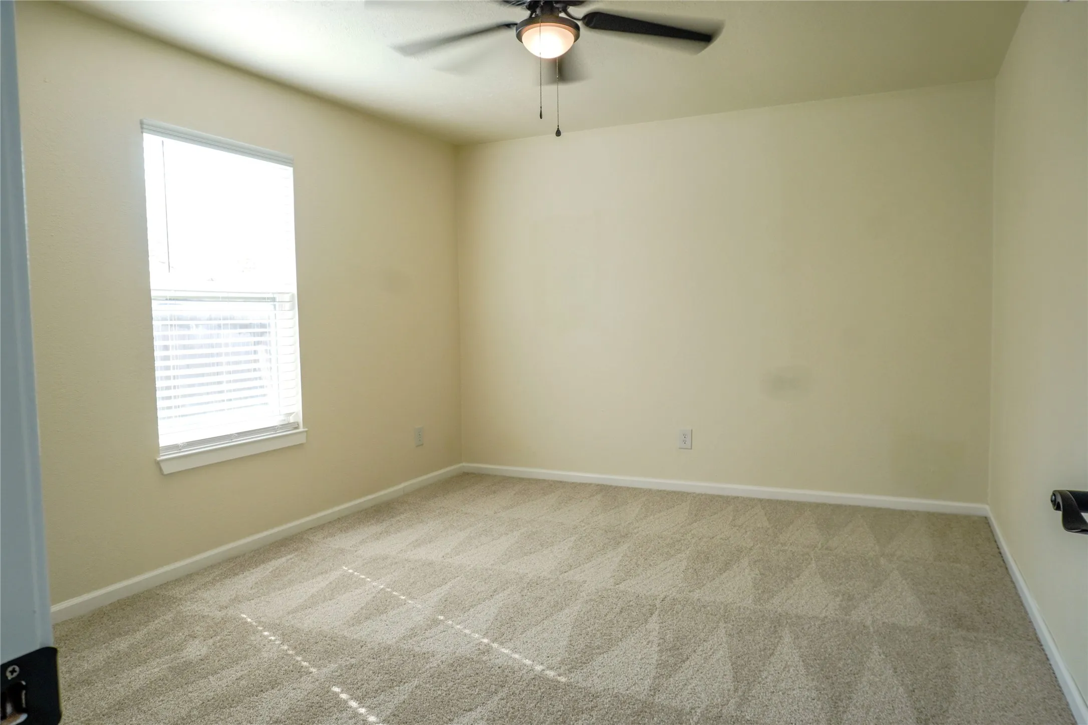 Neutral wall paint, ceiling fan with integrated lighting, window with blinds, and patterned carpet flooring