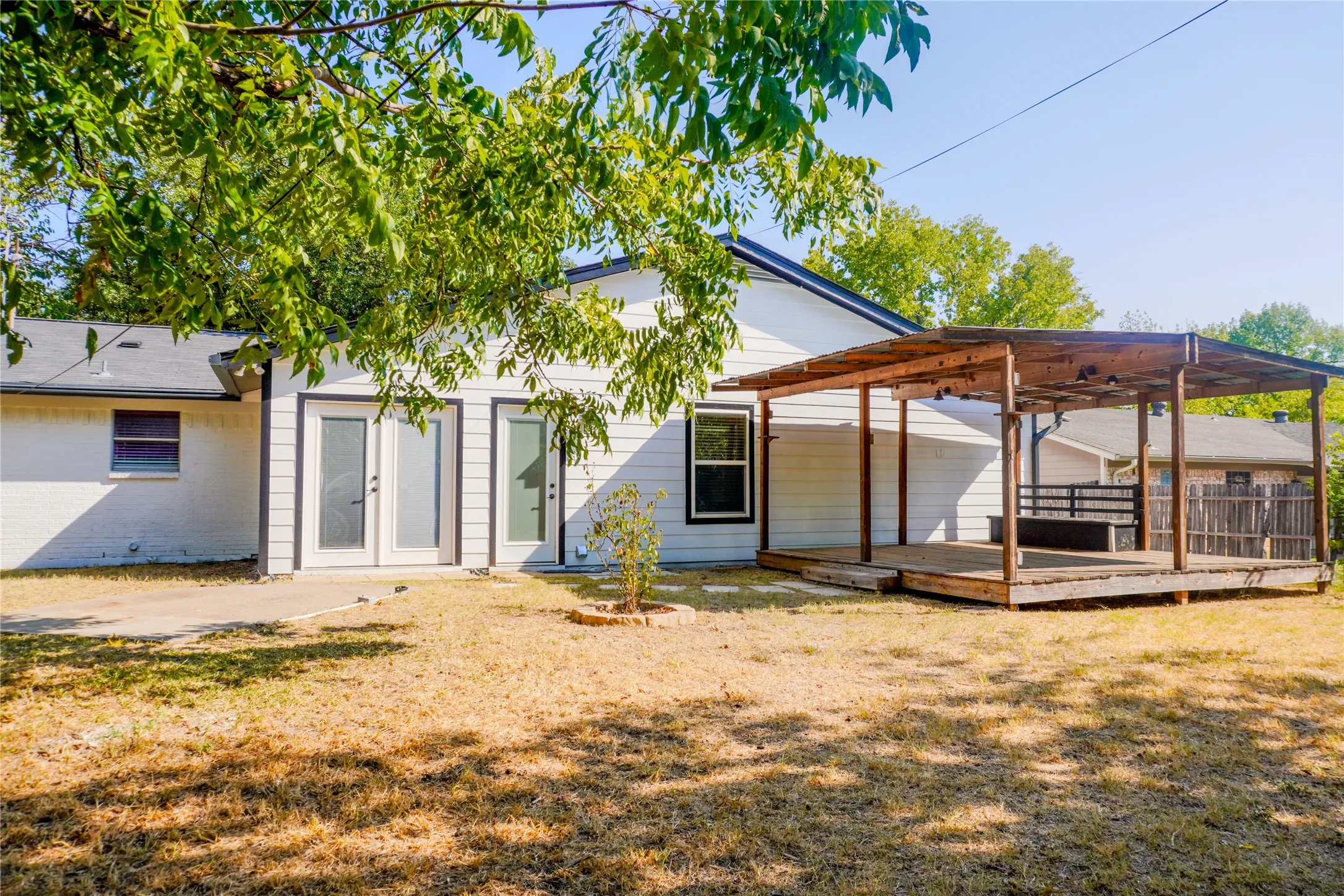 White exterior siding, dual sets of French doors, an expansive wooden deck, and a built-in pergola