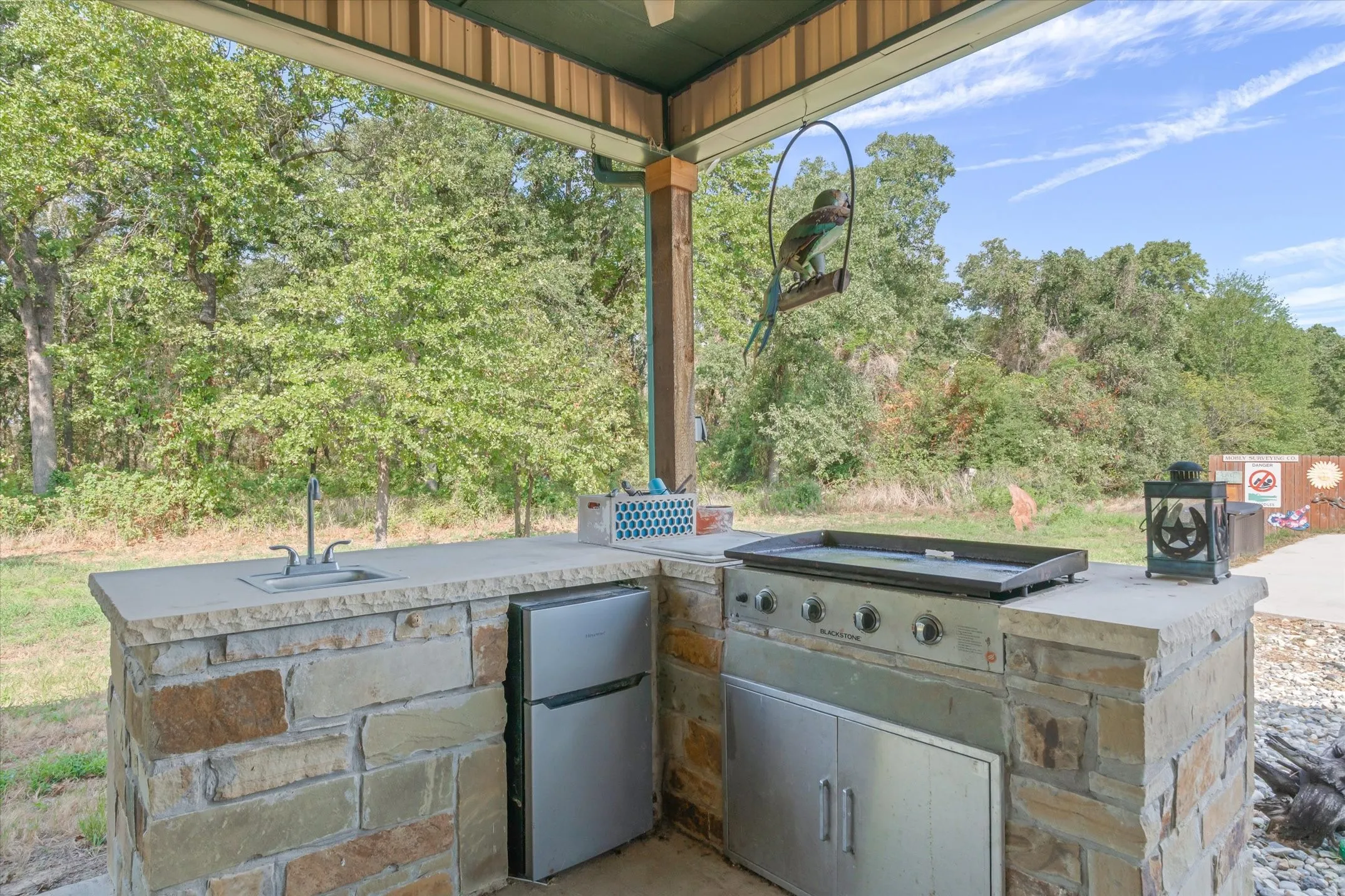 Outddor kitchen has a fridge, griddle, and sink
