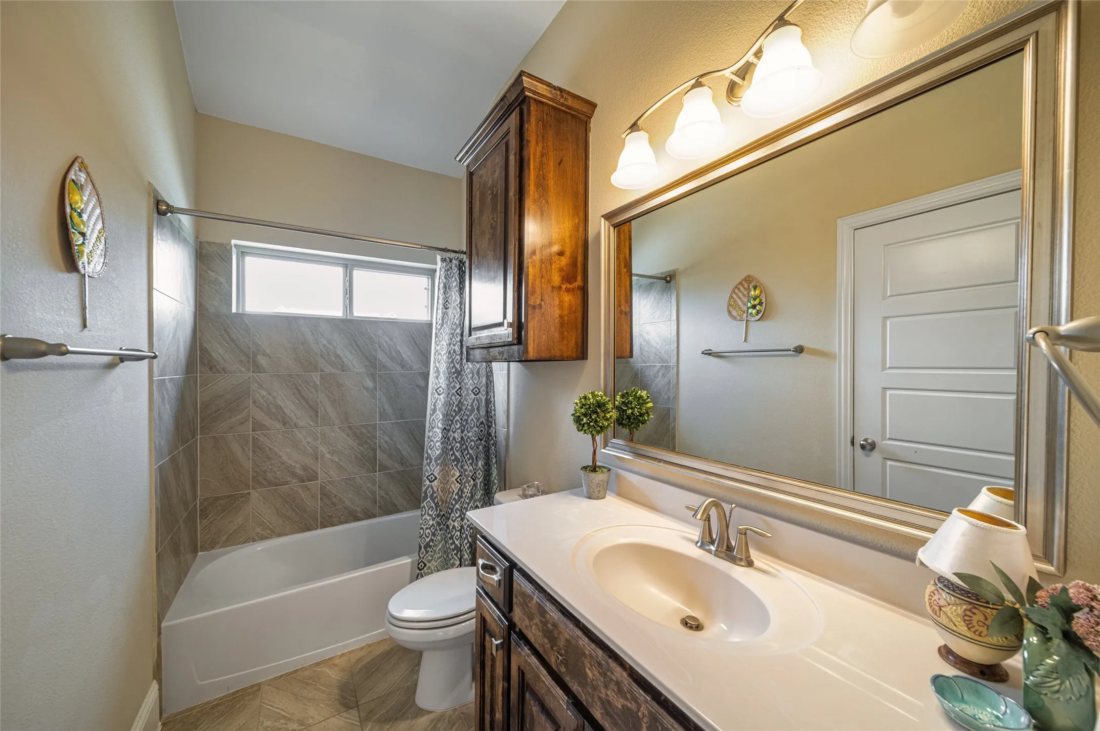 Downstairs 2nd bath Vanity with an integrated sink and brushed nickel faucet, large framed mirror with overhead lighting, a built-in wood-finish cabinet, tiled shower-tub combination, and a window above the tub