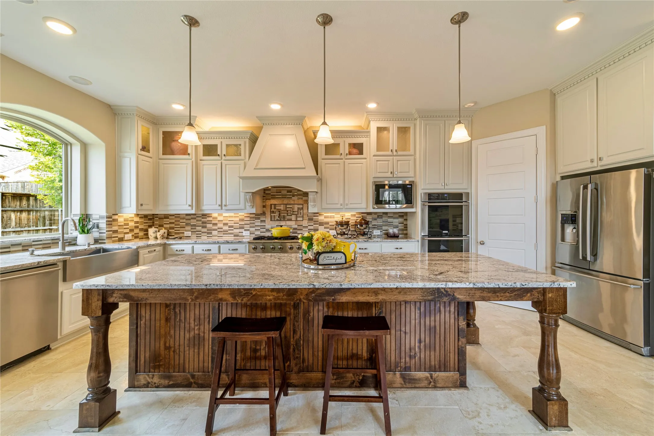 Gourmet kitchen featuring a large wood-paneled island with a granite countertop, stainless steel appliances, white customcabinetry,