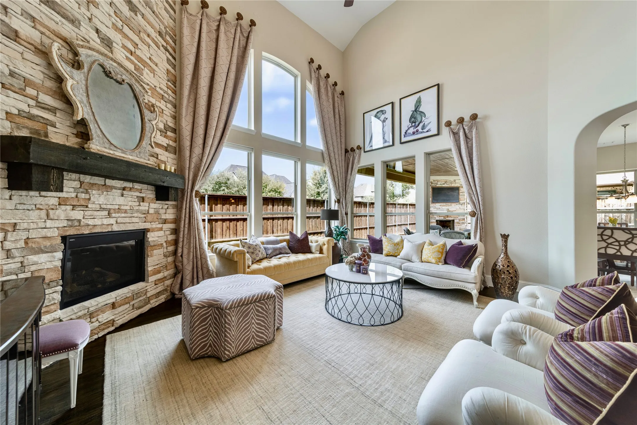 Two-story 20ft ceiling, stone-clad fireplace with wood mantel, arched entryways, large transom windows, and light-toned walls