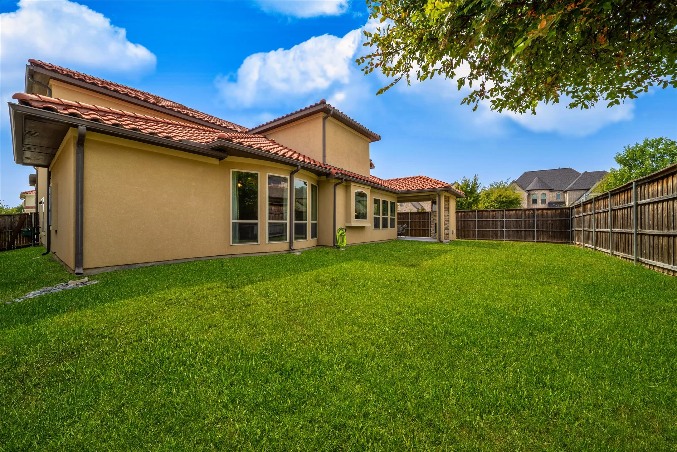 Expansive backyard featuring a manicured lawn, wood fencing, and a covered patio