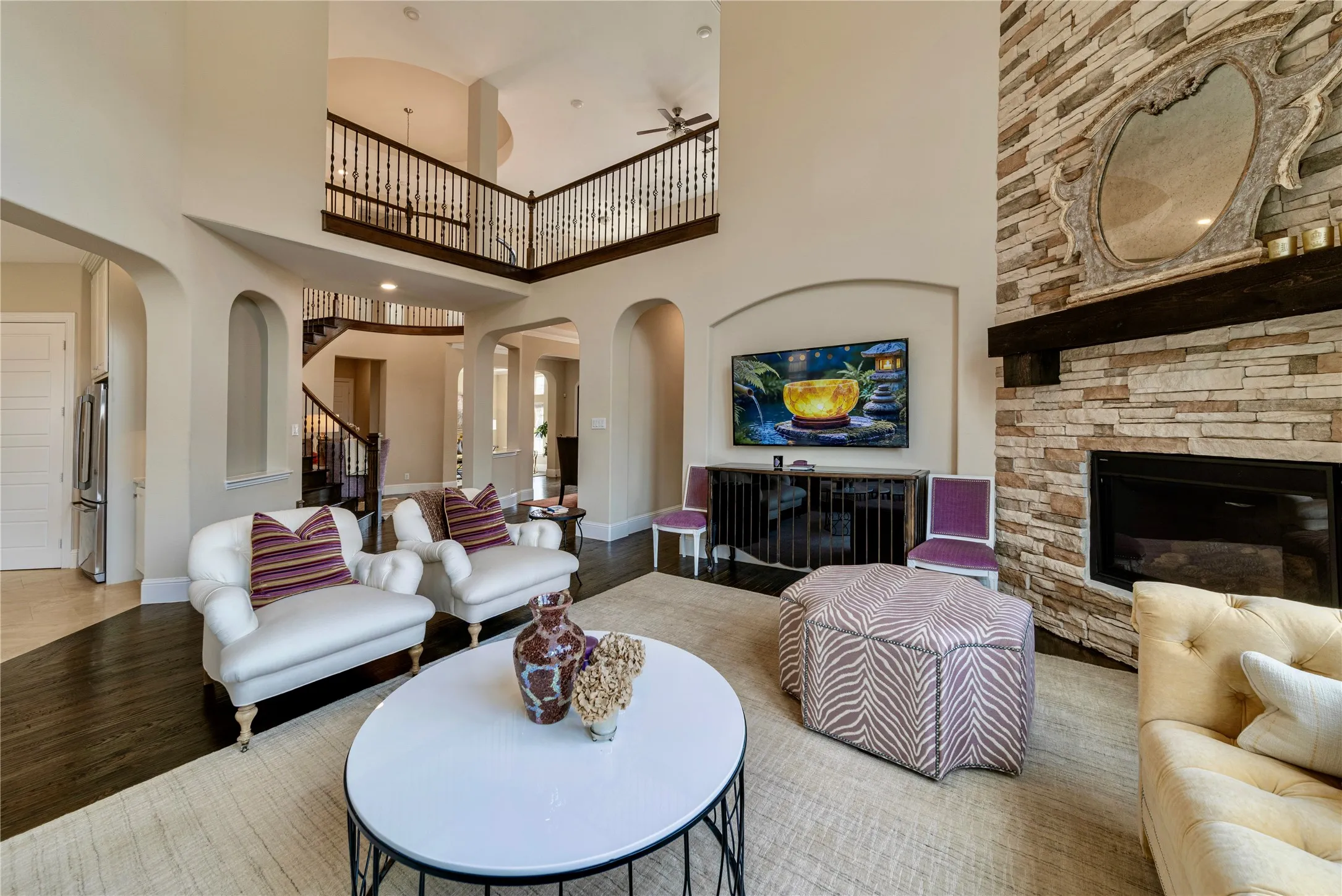 Two-story living area featuring a stone-clad fireplace, dark wood-finish flooring, and arched doorways