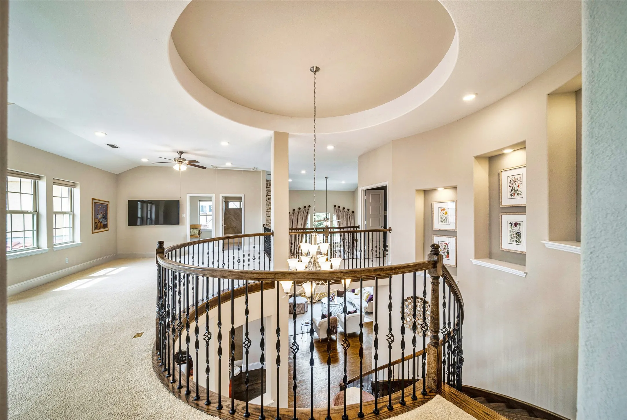 Curved wood-finish handrail with decorative wrought iron spindles, recessed ceiling with accent lighting, built-in wall niches with integrated lighting, vaulted ceiling, and double windows with white trim