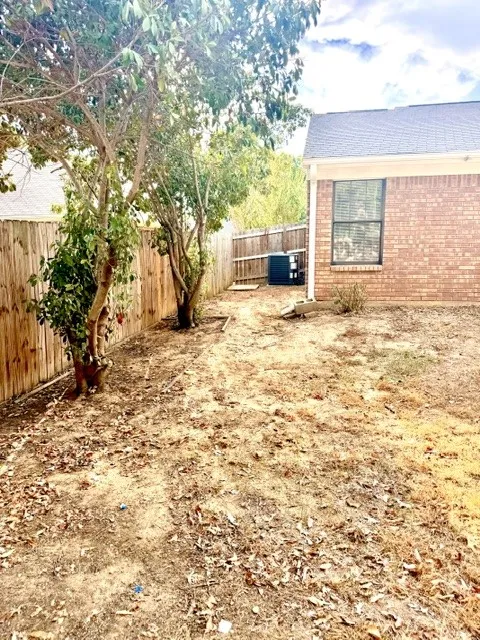 Private backyard space featuring a wood fence, mature trees, and a brick-clad exterior wall with a window