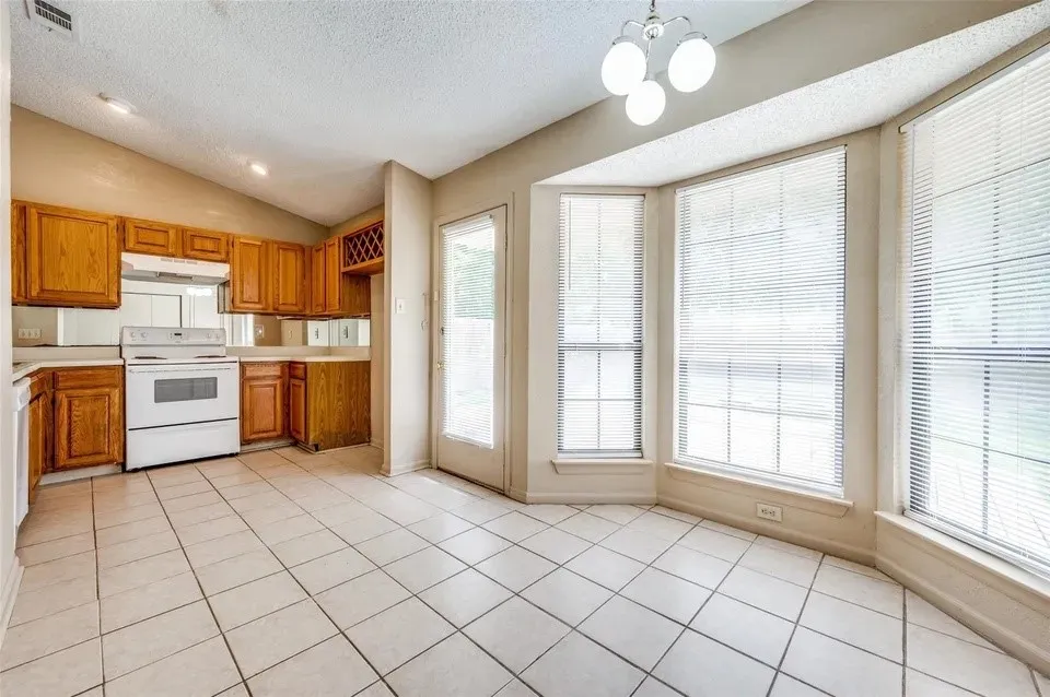 Kitchen featuring natural wood cabinetry, white appliances, tile flooring, and a bay window