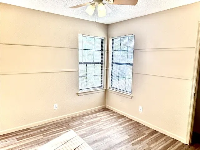 Wood-finish flooring, two large windows with blinds, chair rail molding, ceiling fan with integrated lighting