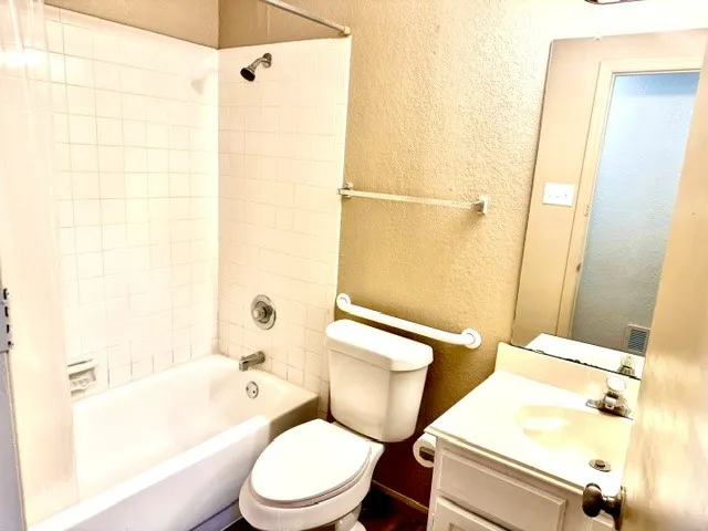 Bathroom featuring a built-in tub with tile surround, a single vanity with storage, and a wall-mounted mirror
