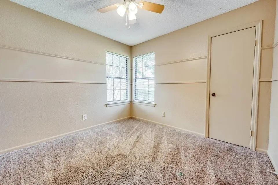 Textured wall finish with decorative chair rail molding, corner windows, neutral carpeting, and a ceiling fan