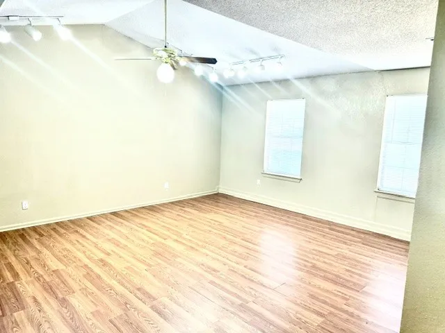 Vaulted ceiling with a ceiling fan, wood-finish flooring, and track lighting