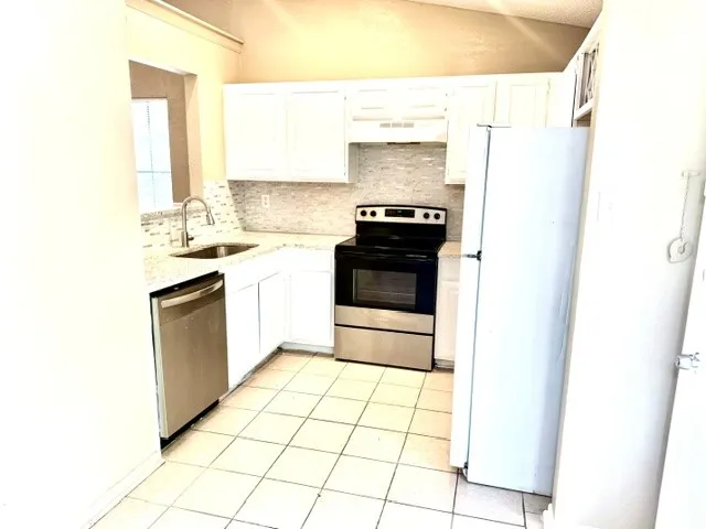Kitchen featuring white cabinetry, stone-finish countertops, stainless steel appliances, and a tiled backsplash