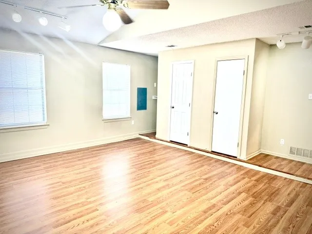 Wood-finish flooring throughout, multiple windows with blinds, ceiling fan, and track lighting