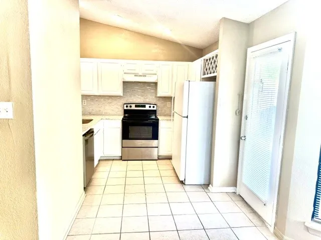 Kitchen featuring white cabinetry, tile flooring, stainless steel appliances, and a vaulted ceiling