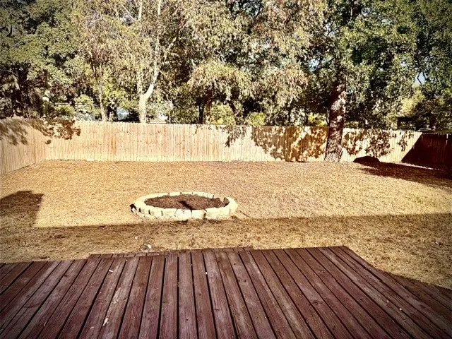 Spacious backyard with a wood privacy fence, stone fire pit, mature trees, and a wood deck