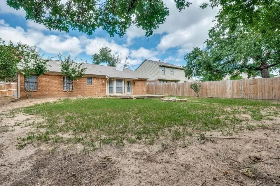 Expansive backyard featuring a wood privacy fence, a wooden deck, and a brick exterior with multiple windows