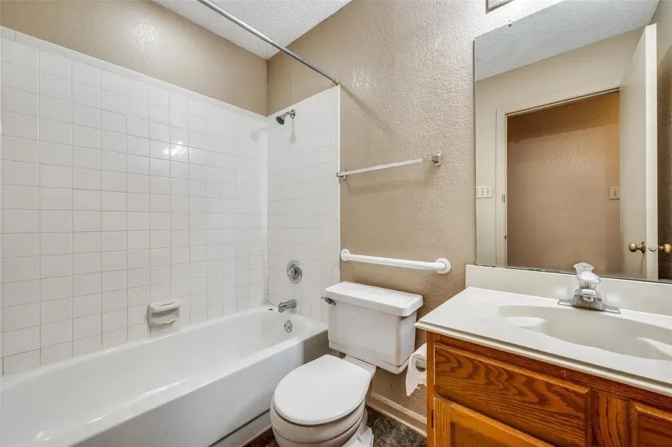 Tub-shower combination with white tile surround, wood-finish vanity, and integrated sink