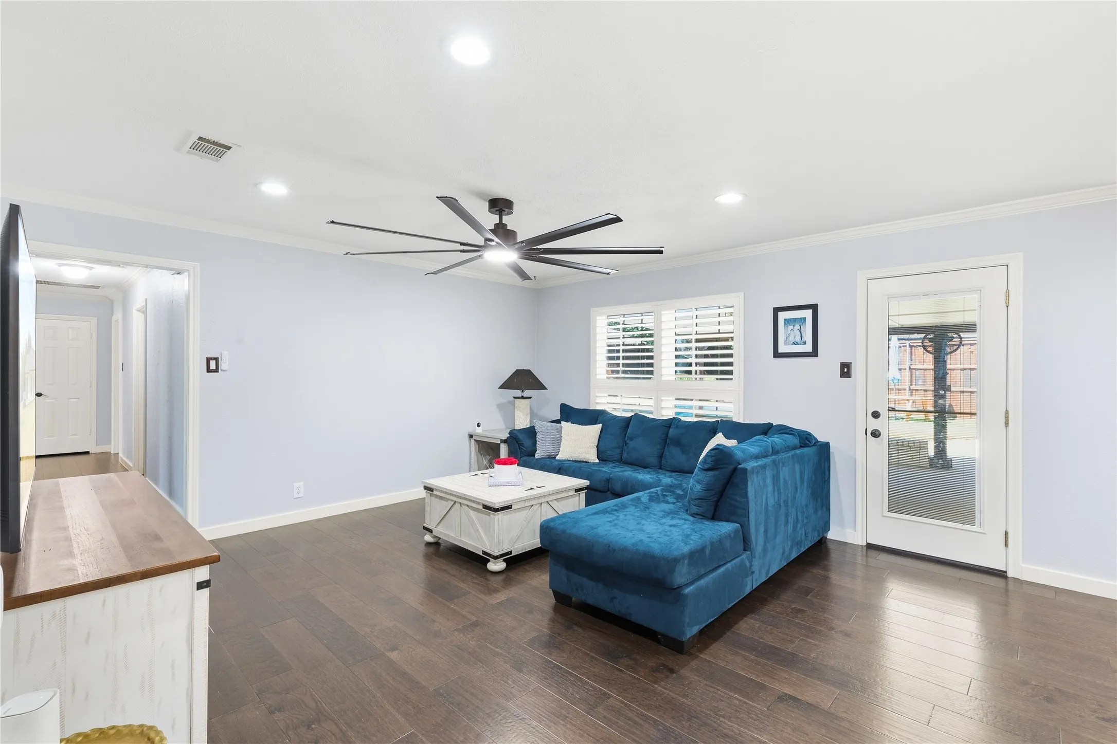 Spacious living area featuring wood-finish flooring, recessed lighting, crown molding, a modern ceiling fan, and a glass-paneled exterior door