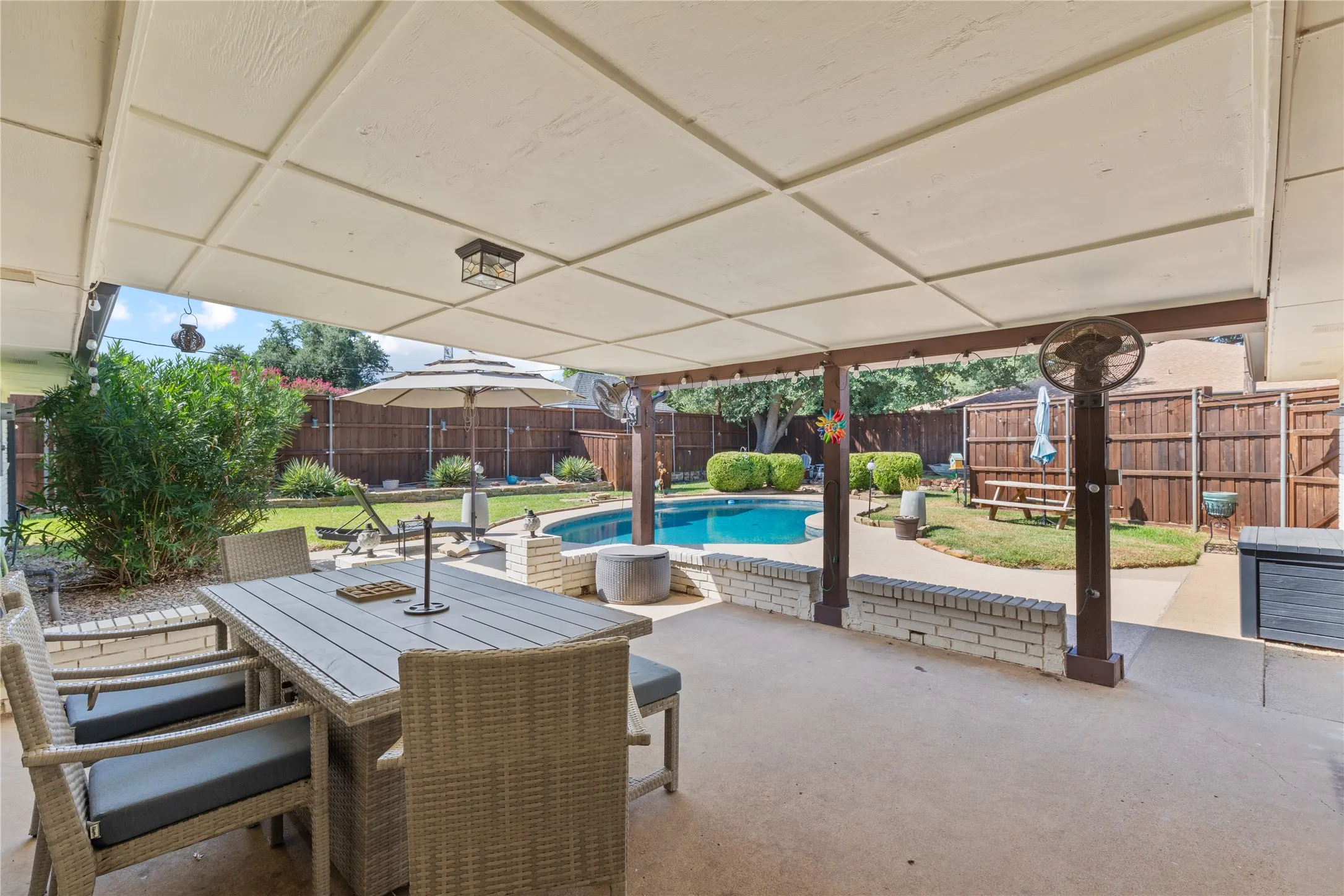 Covered patio with concrete flooring, wood support beams, and an in-ground swimming pool