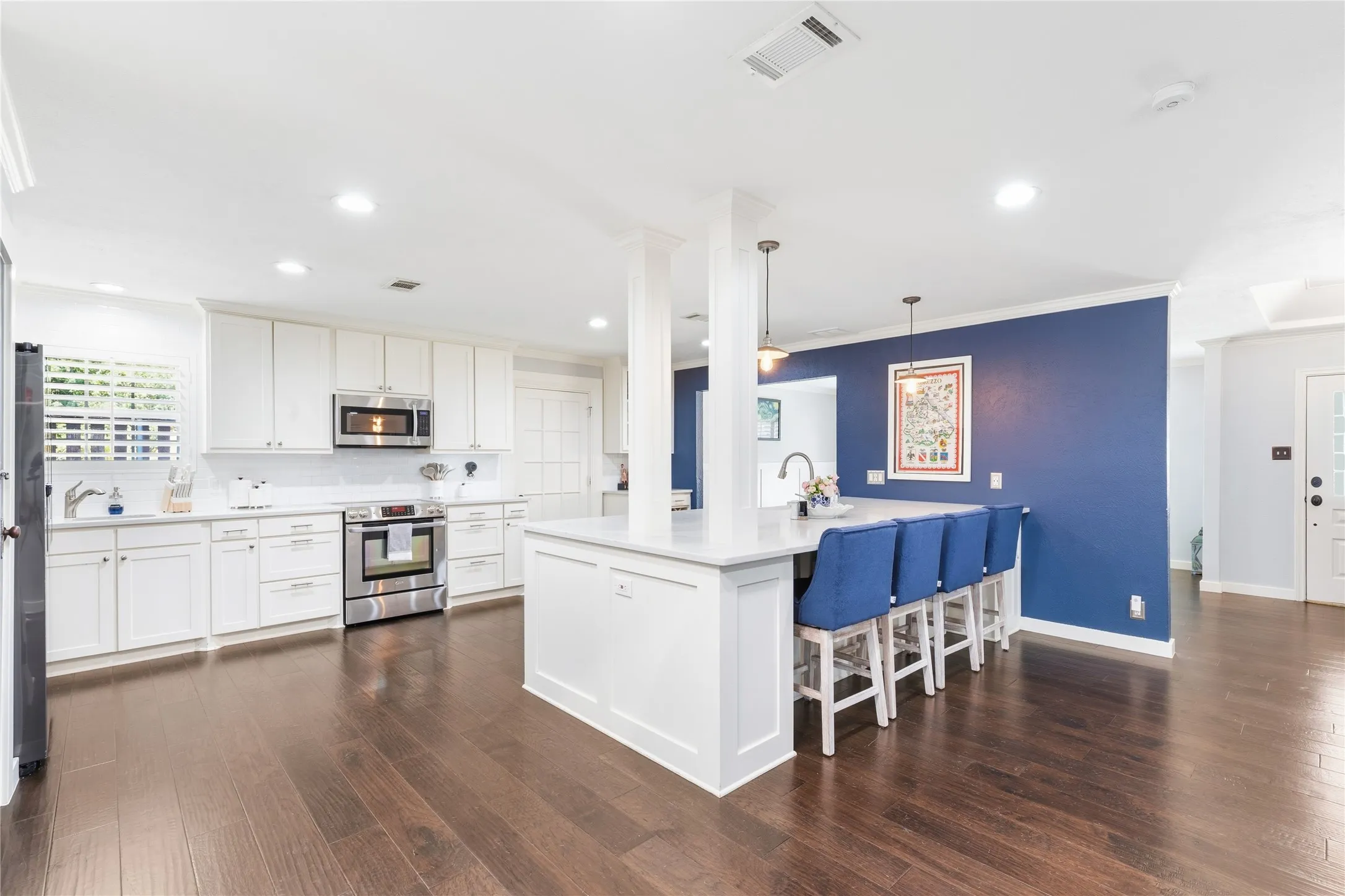 Gourmet kitchen with white cabinetry, stainless steel appliances, large center island with seating, and wood-finish flooring