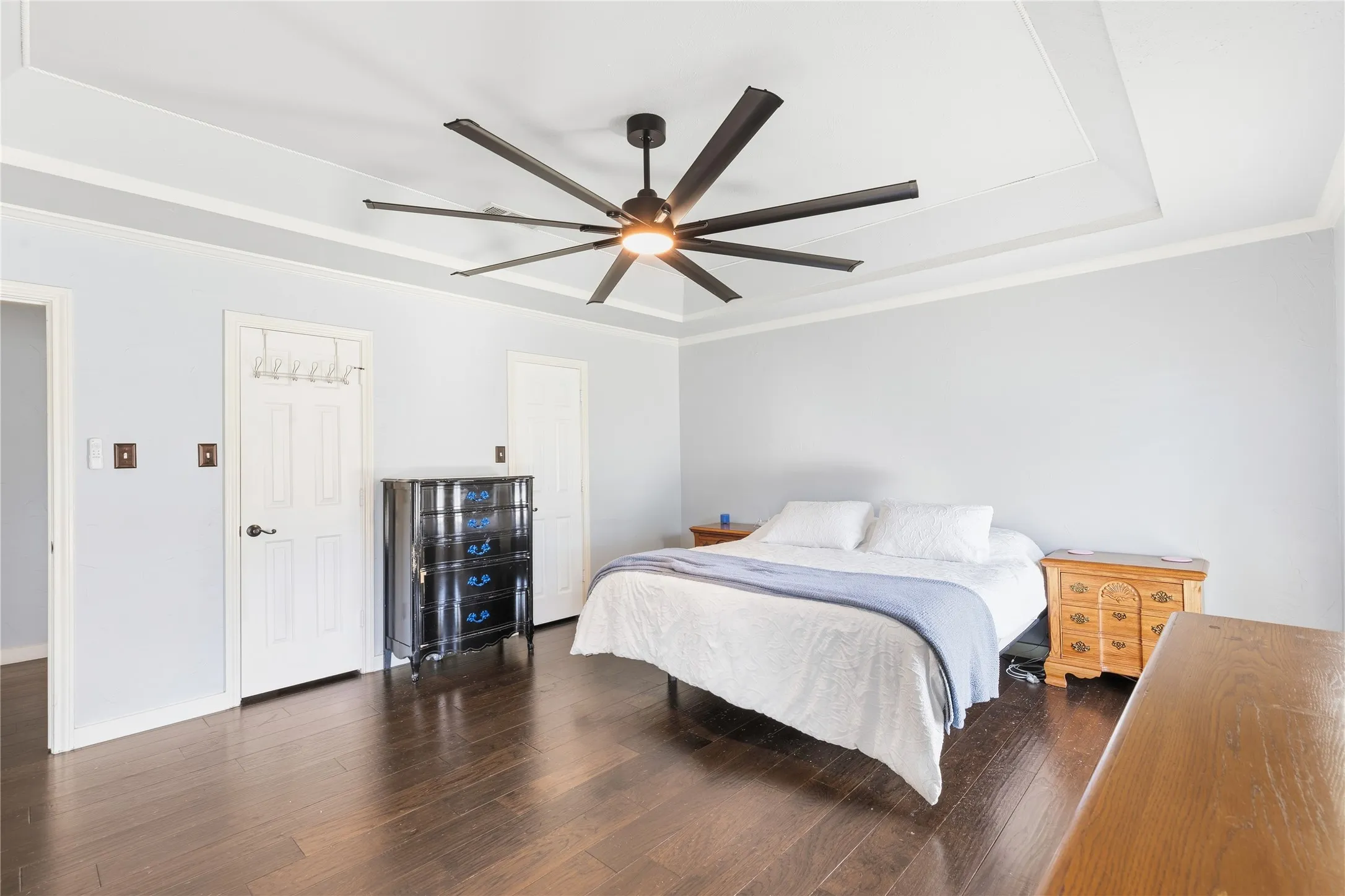 Tray ceiling with crown molding, dark wood-finish flooring, white paneled doors, and a multi-blade ceiling fan