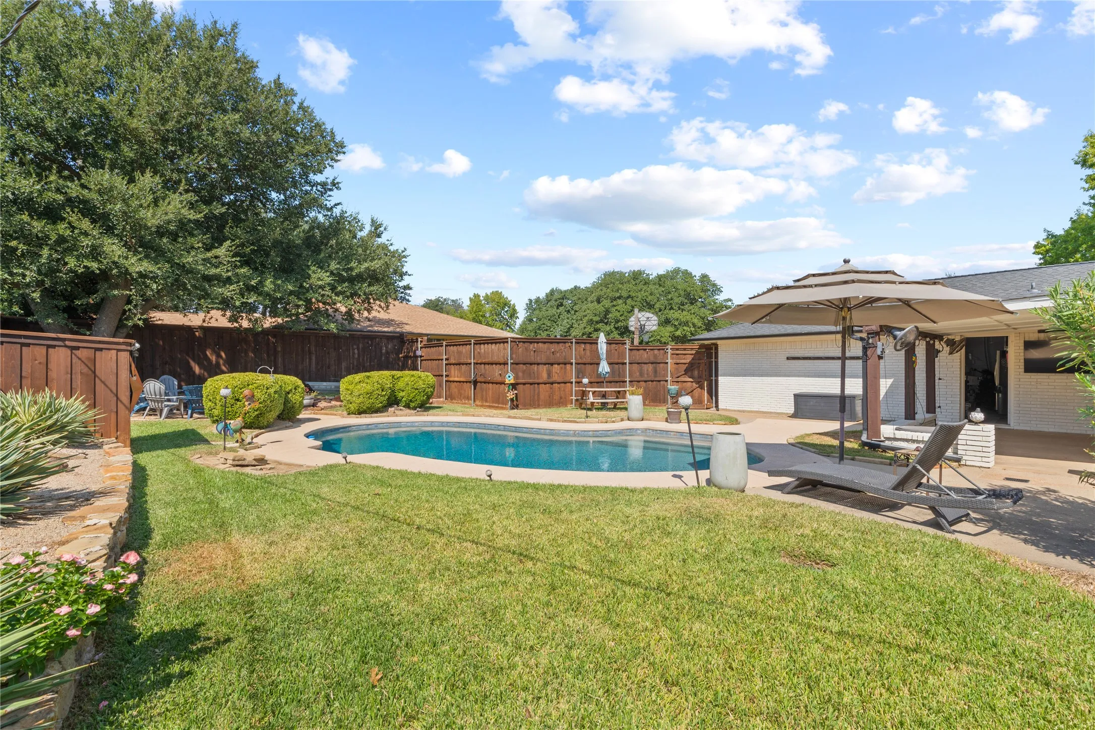Private backyard featuring a swimming pool, concrete patio, and lush green lawn