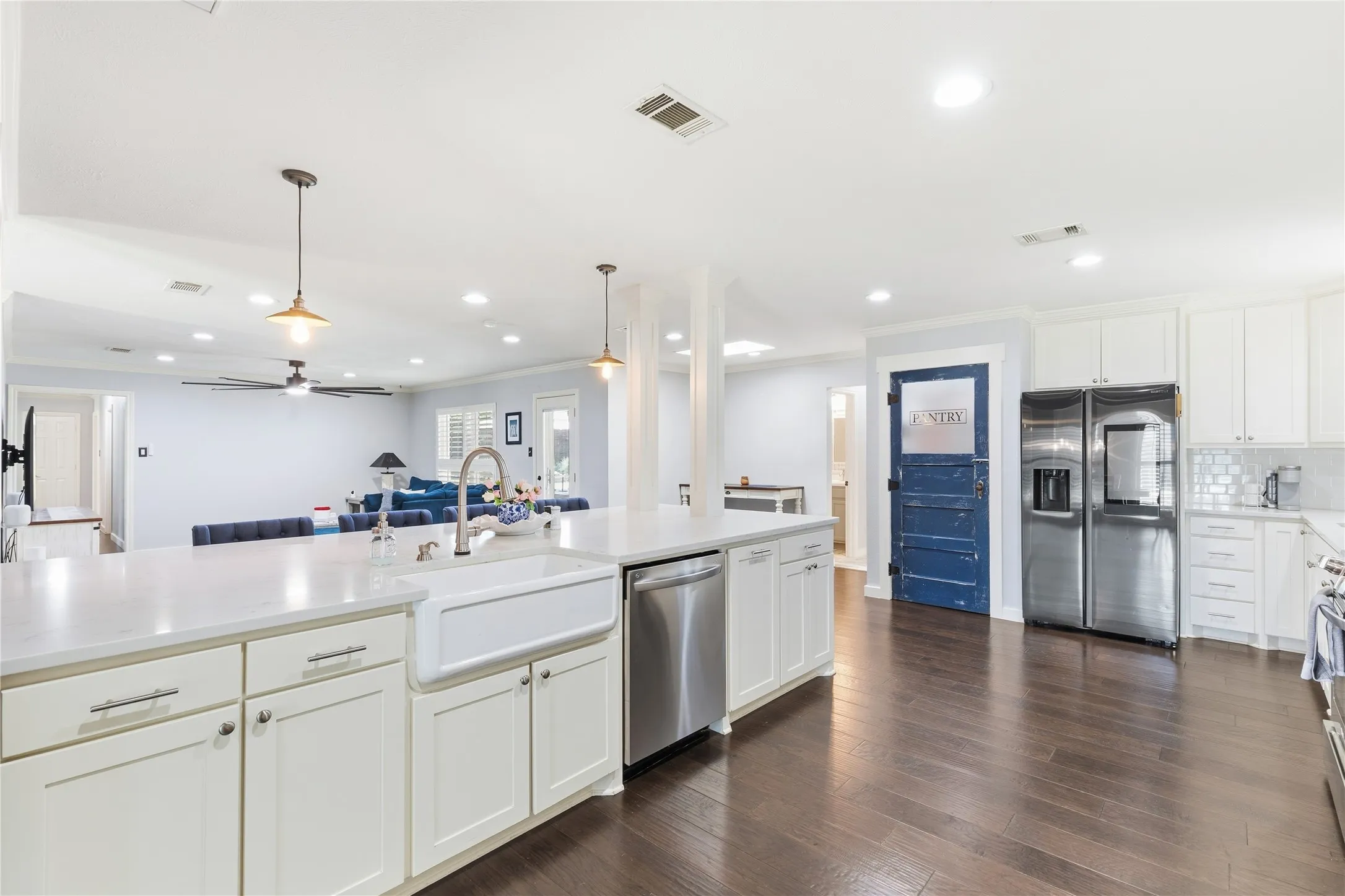 Spacious kitchen featuring an expansive island with a farmhouse sink, white cabinetry, dark wood-finish flooring, and a subway tile backsplash
