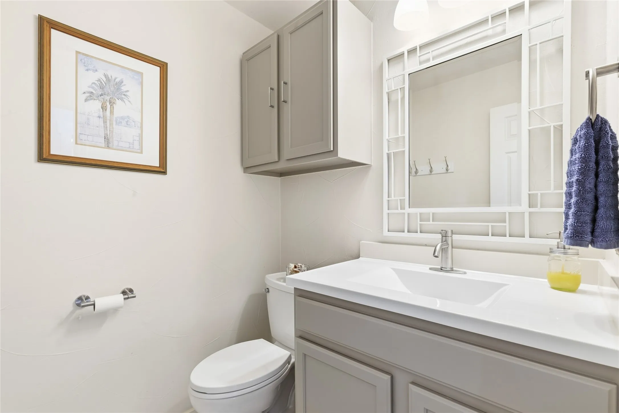 White vanity with an integrated rectangular sink, gray base cabinetry, and an ornate framed mirror