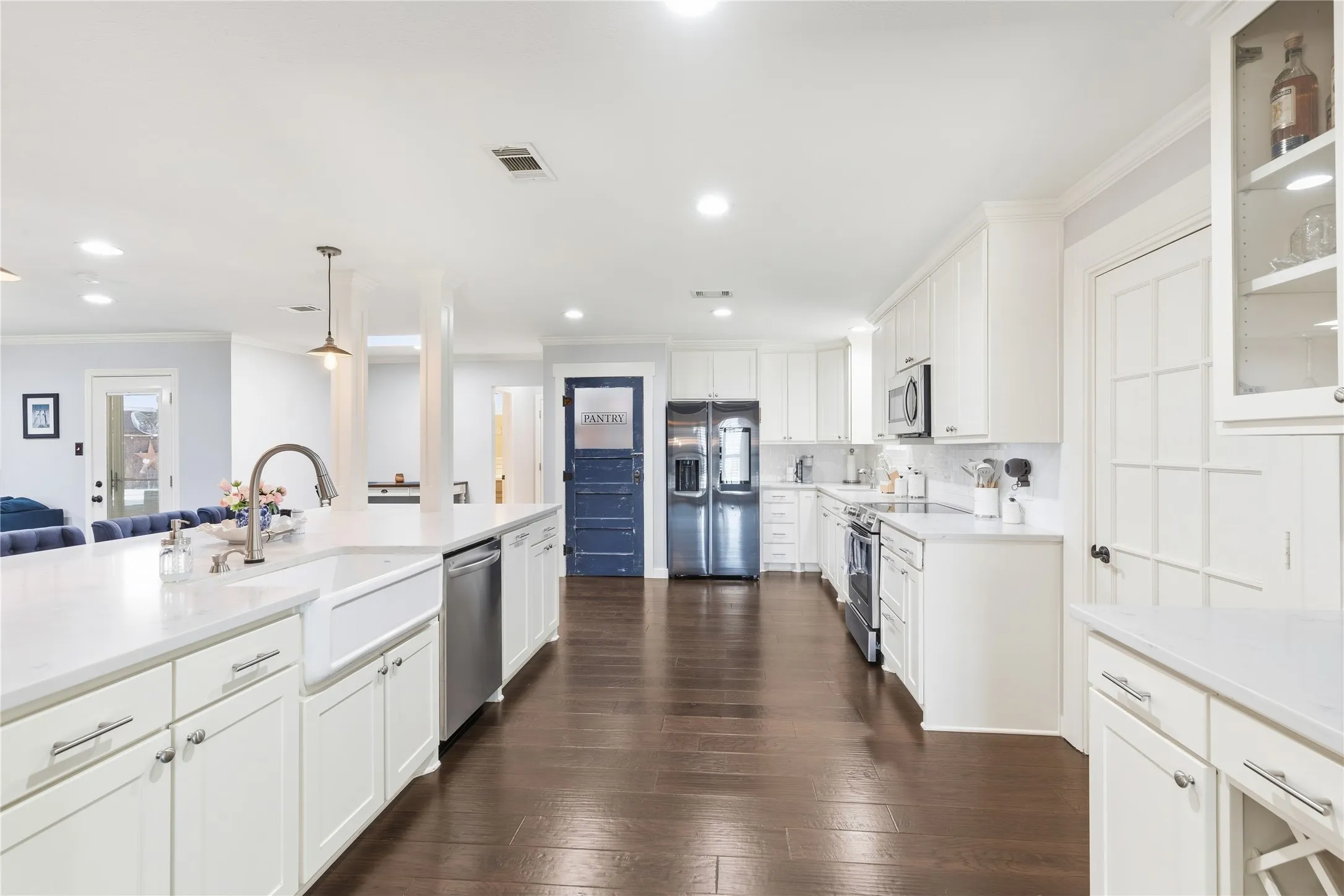 White shaker-style cabinetry with chrome hardware, dark wood-finish flooring, stainless steel appliances, white farmhouse sink with gooseneck faucet, and white countertops