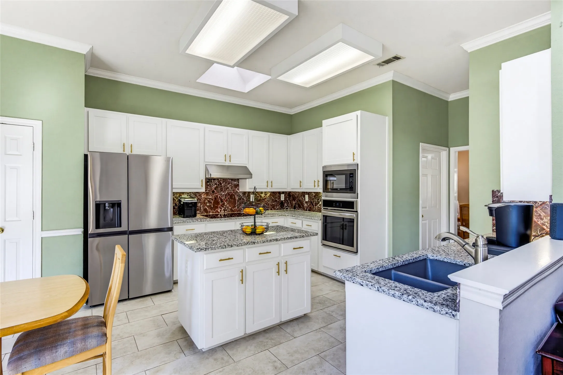White cabinetry with modern gold-finish hardware, granite countertops, stainless steel appliances, a center island, and tile flooring. Kitchen remodeled in 2023. This amazing refrigerator stays.....it even produces ROUND ice cubes for your grown up drinks!!