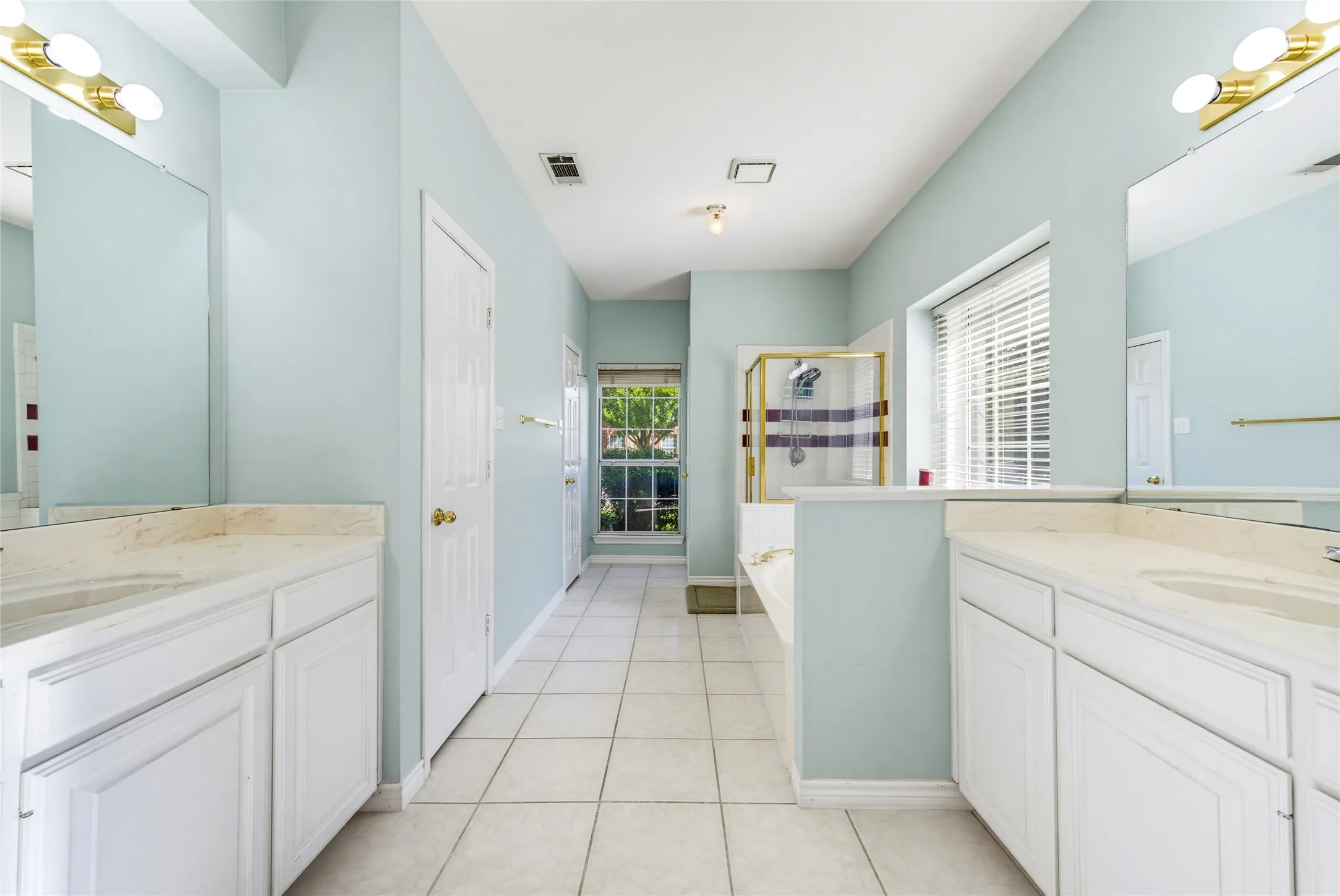 Dual vanity setup with white cabinetry and light-colored countertops and tile flooring....