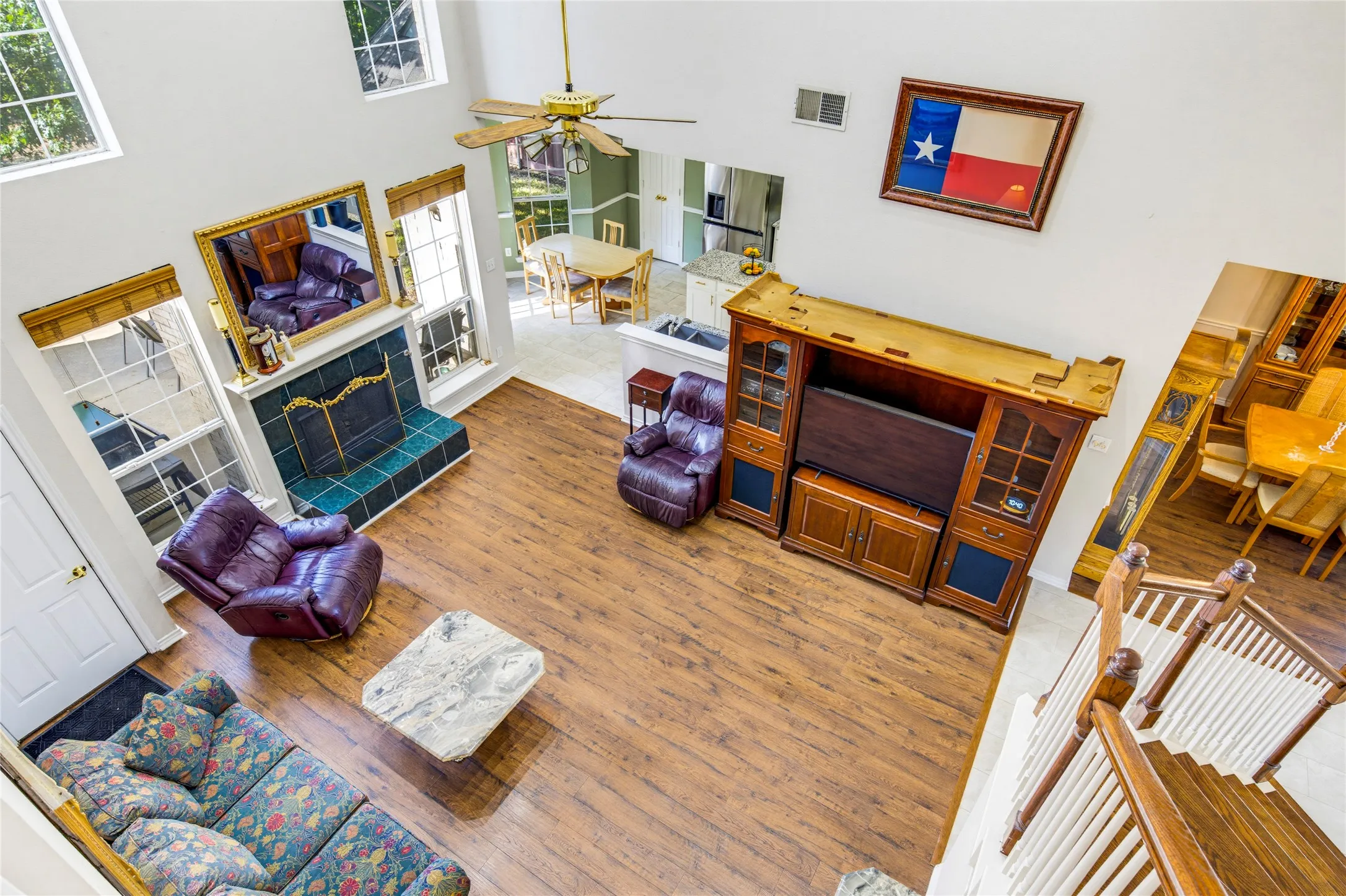 Two-story living area with wood look laminate flooring, a tiled fireplace, a ceiling fan and lots of natural light

