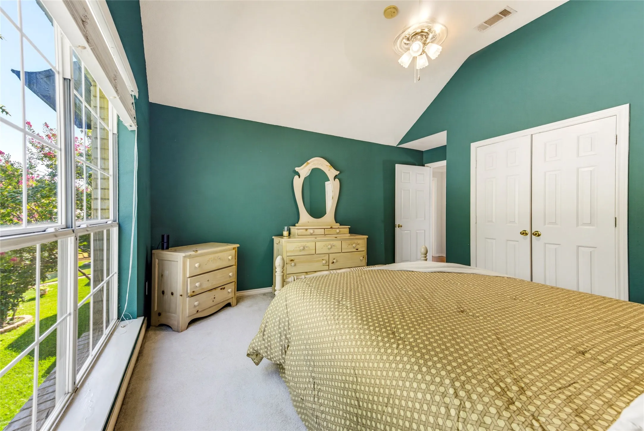 Vaulted ceiling, carpeted flooring, large window with multi-pane design, double-door closet, and ceiling fan with light fixture....